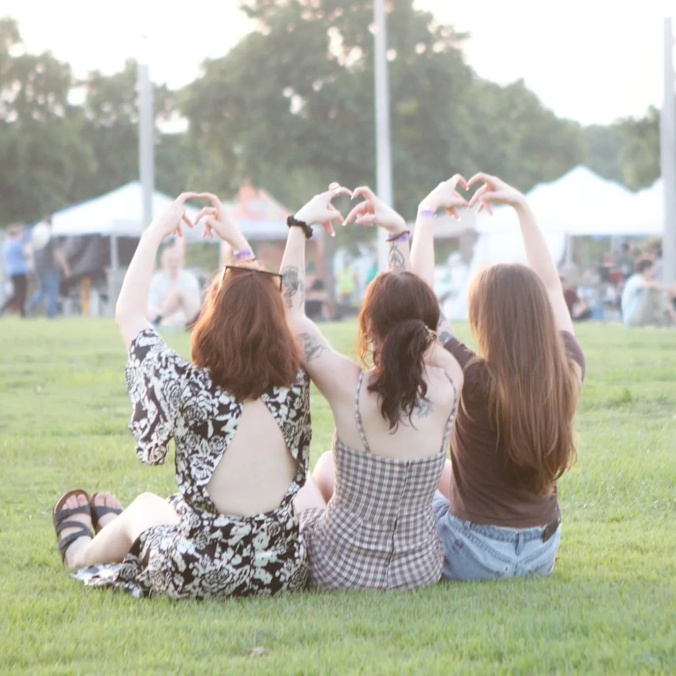 Three friends making heart shapes with their hands on the lawn at Asian Night Market Memphis 2025
