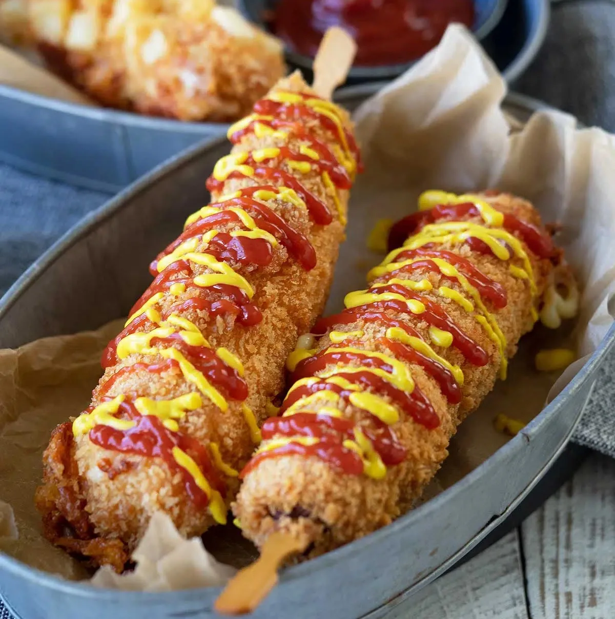Two crispy Korean corn dogs drizzled with ketchup and mustard
