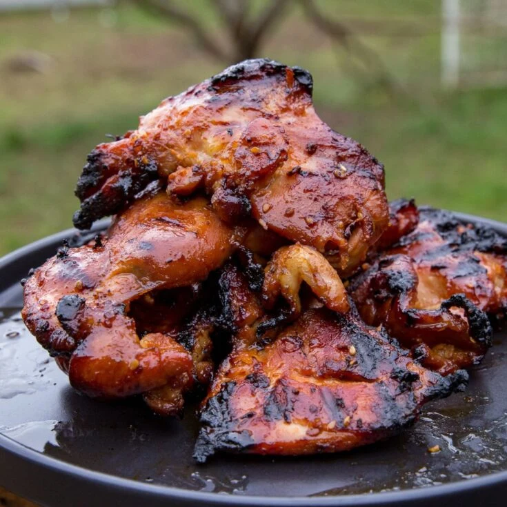 Char-grilled teriyaki chicken thighs with a glossy sweet-soy glaze piled on a black plate