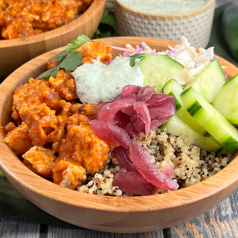 Chicken tikka bowl with quinoa, cucumber, pickled onions, and herbed yogurt in a wooden bowl